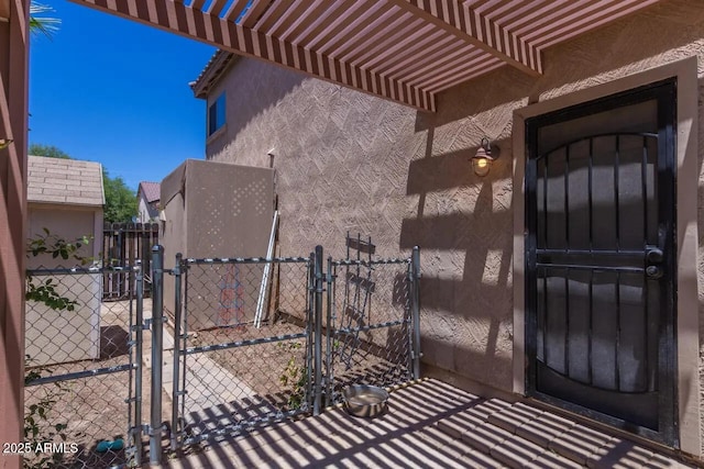 property entrance with stucco siding, a pergola, fence, and a gate