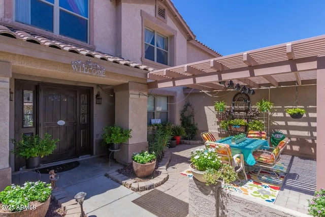 doorway to property featuring a tiled roof, a patio area, a pergola, and stucco siding