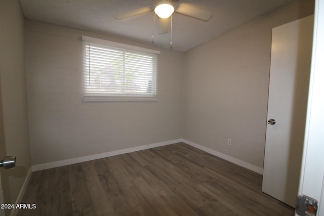 spare room with dark hardwood / wood-style floors, a textured ceiling, brick wall, and ceiling fan