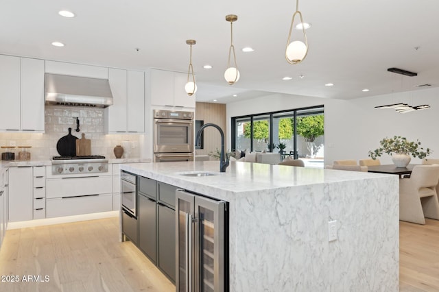 kitchen featuring wall chimney range hood, wine cooler, modern cabinets, and a sink