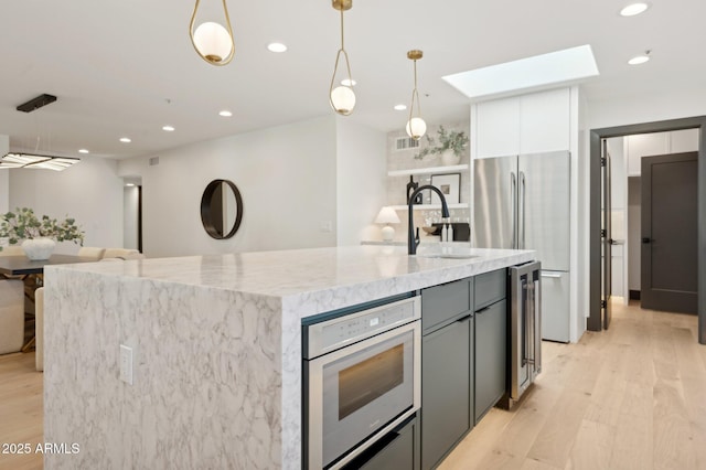 kitchen featuring oven, light wood-style flooring, freestanding refrigerator, a skylight, and light stone countertops