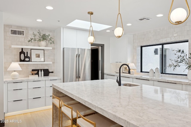 kitchen featuring visible vents, light stone countertops, freestanding refrigerator, and a sink