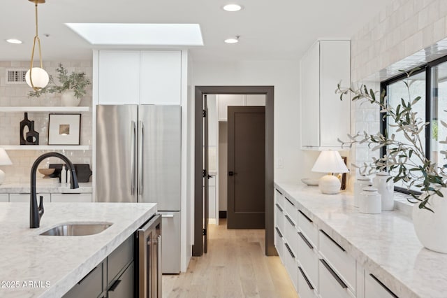 kitchen with wine cooler, light wood-type flooring, light stone counters, freestanding refrigerator, and a sink