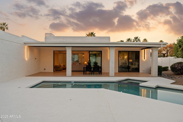 back of property at dusk with a patio, a fenced in pool, fence, and an in ground hot tub