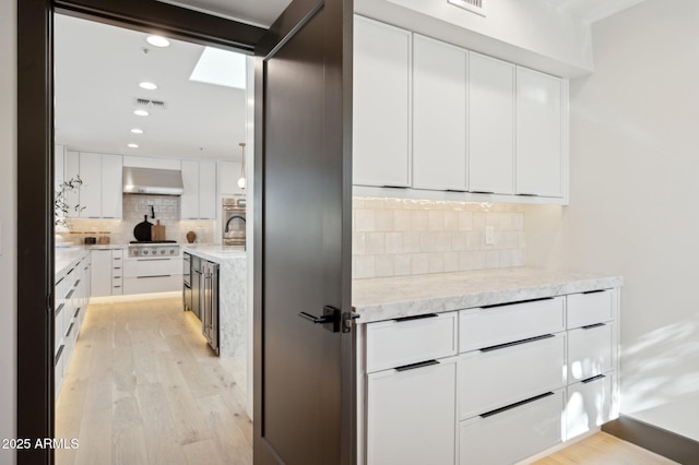 kitchen with visible vents, white cabinets, wall chimney exhaust hood, light wood-type flooring, and backsplash