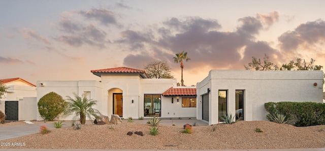 view of front facade with a tiled roof, an attached garage, driveway, and stucco siding
