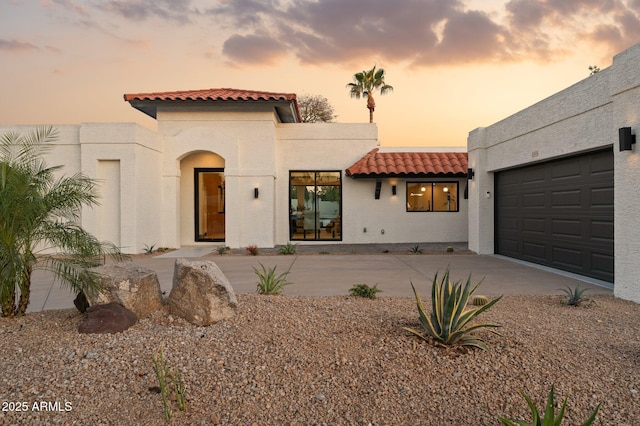 mediterranean / spanish-style home with a garage, concrete driveway, stucco siding, and a tile roof