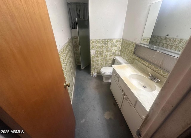 half bathroom featuring vanity, a wainscoted wall, concrete flooring, tile walls, and toilet