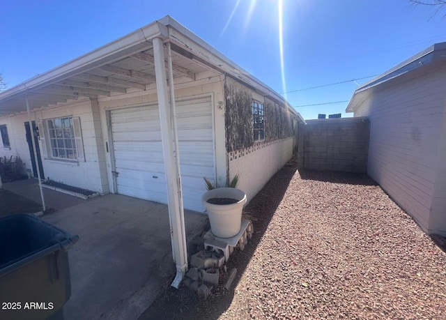 view of side of home featuring concrete block siding, an attached garage, and fence