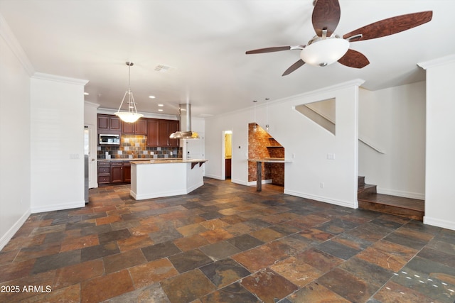 kitchen featuring pendant lighting, backsplash, island range hood, ornamental molding, and a center island with sink