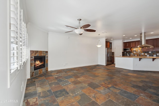 unfurnished living room with a tiled fireplace, ornamental molding, and ceiling fan