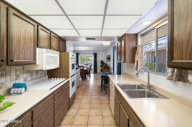 kitchen with tasteful backsplash, light tile patterned flooring, sink, a drop ceiling, and white appliances