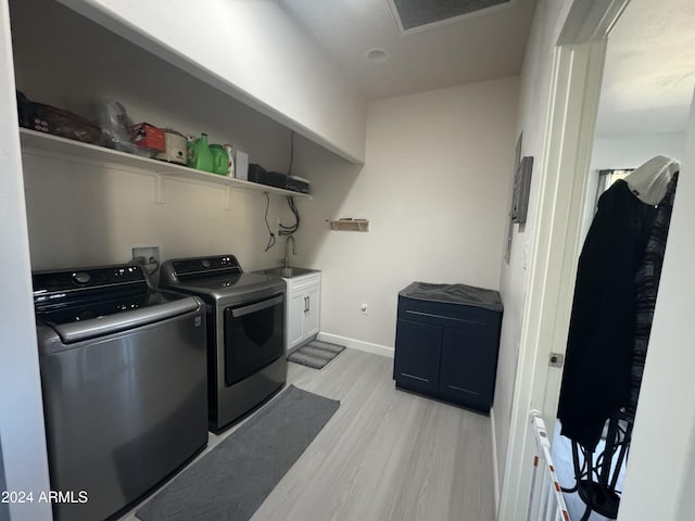 laundry room with cabinets, washing machine and dryer, sink, and light hardwood / wood-style flooring