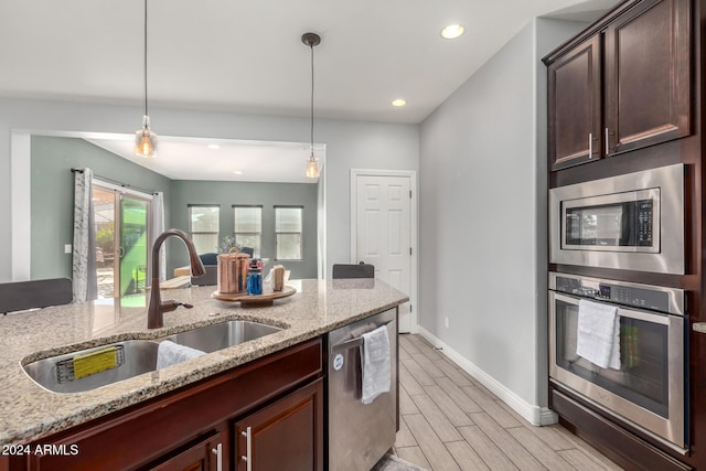 kitchen featuring sink, light wood-type flooring, decorative light fixtures, light stone counters, and stainless steel appliances