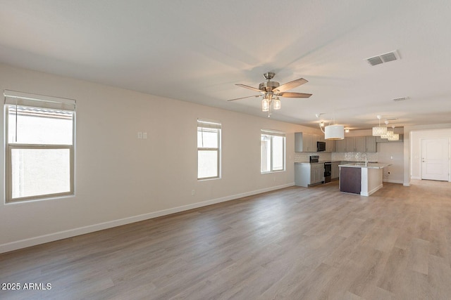 unfurnished living room featuring a sink, baseboards, visible vents, and light wood-type flooring