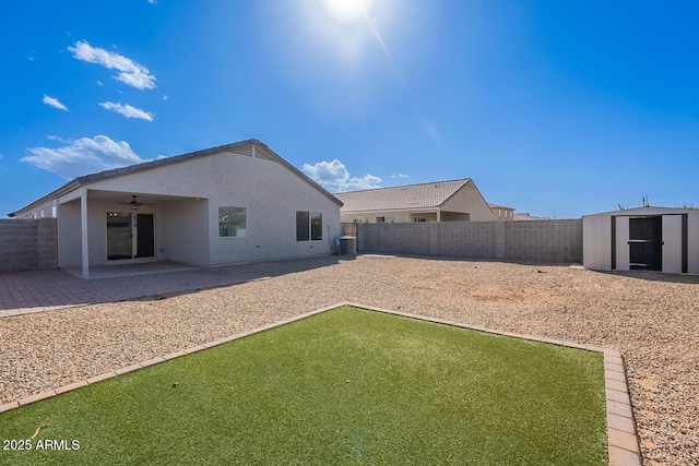 back of house featuring a storage shed, a fenced backyard, an outdoor structure, a ceiling fan, and a patio