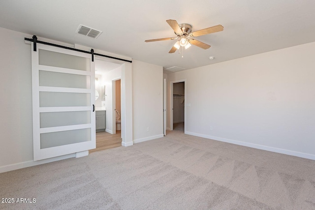 unfurnished bedroom with baseboards, visible vents, a spacious closet, light carpet, and a barn door