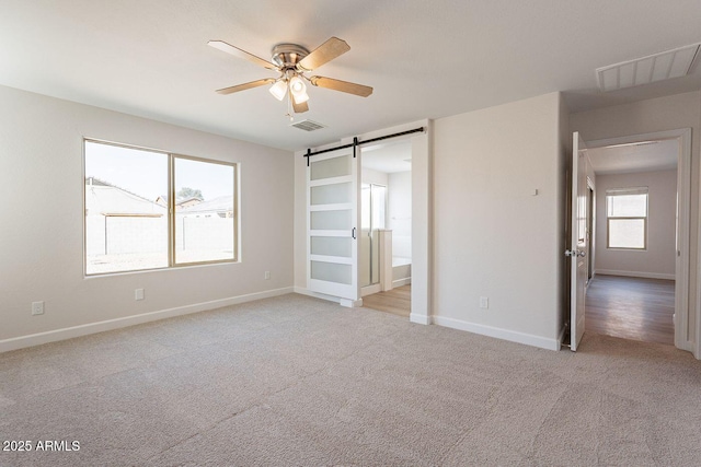 unfurnished bedroom with a barn door, baseboards, visible vents, and light carpet