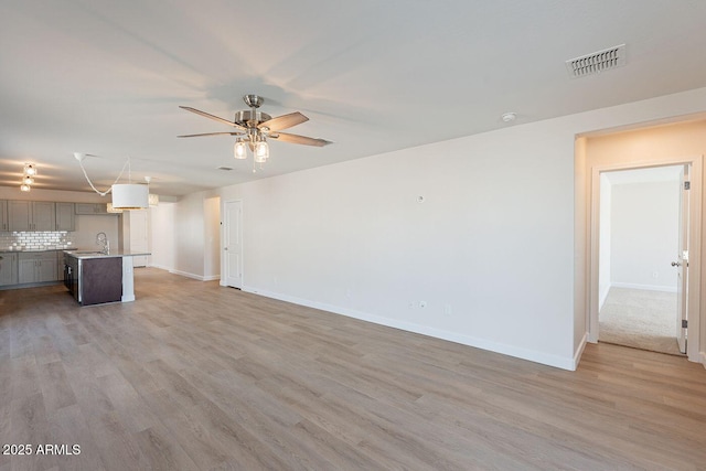 unfurnished living room featuring ceiling fan, light wood-style flooring, visible vents, and a sink