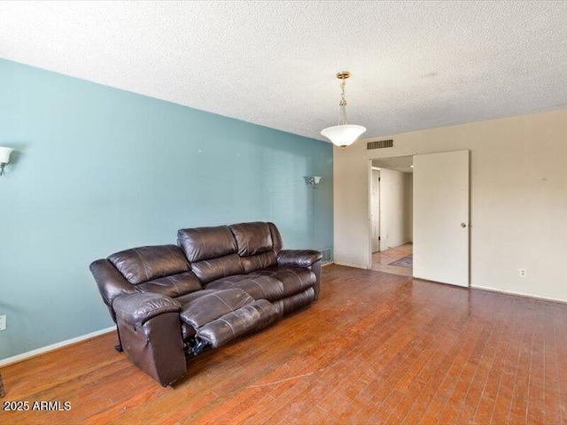 living room with baseboards, a textured ceiling, visible vents, and wood finished floors