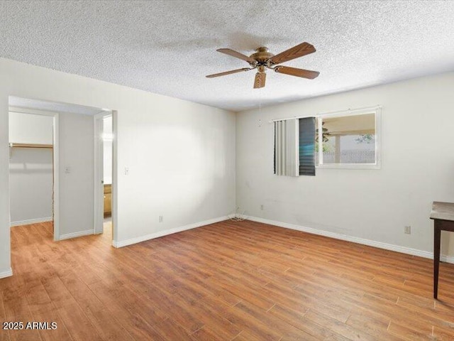 unfurnished bedroom with a closet, a spacious closet, a textured ceiling, wood finished floors, and baseboards