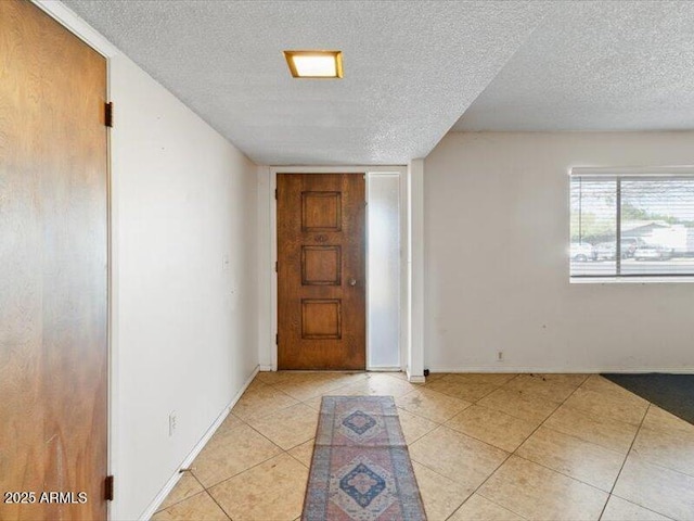 entryway with a textured ceiling, baseboards, and light tile patterned floors