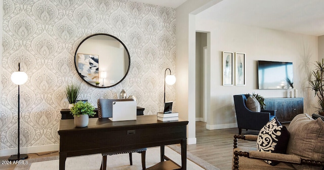 office featuring wallpapered walls, an accent wall, baseboards, and wood finished floors