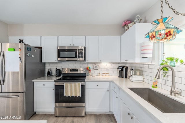 kitchen with light wood finished floors, a sink, stainless steel appliances, white cabinets, and tasteful backsplash