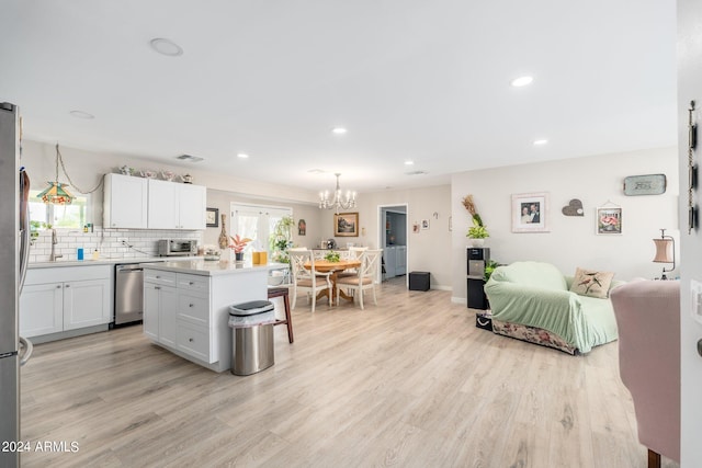 kitchen with appliances with stainless steel finishes, a center island, hanging light fixtures, white cabinetry, and light wood-type flooring