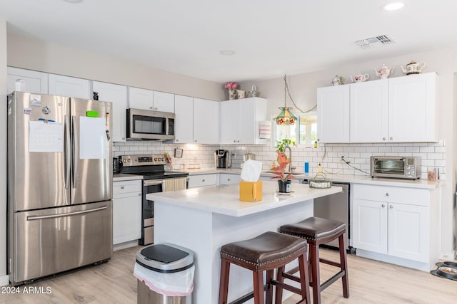 kitchen featuring light hardwood / wood-style flooring, a kitchen bar, a center island, stainless steel appliances, and decorative backsplash