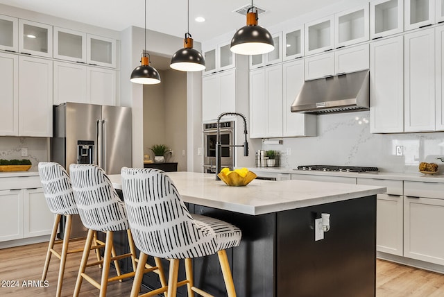 kitchen with light stone counters, a kitchen island with sink, light hardwood / wood-style flooring, exhaust hood, and stainless steel appliances