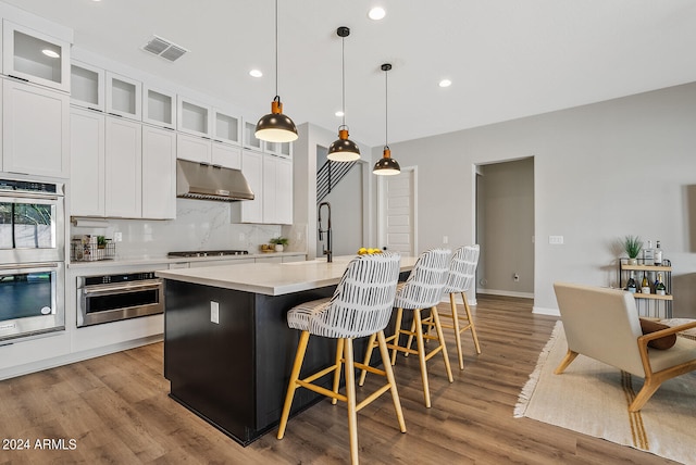 kitchen featuring pendant lighting, an island with sink, light wood-type flooring, and extractor fan