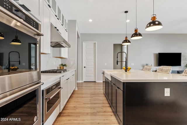 kitchen with a breakfast bar area, an island with sink, white cabinets, hanging light fixtures, and appliances with stainless steel finishes