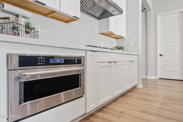 kitchen with wall chimney exhaust hood, white cabinets, light hardwood / wood-style flooring, and stainless steel oven