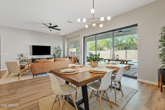 dining space with ceiling fan with notable chandelier and light hardwood / wood-style flooring