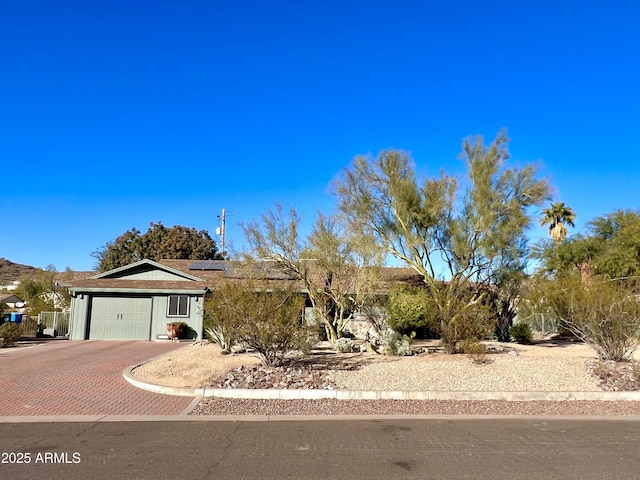 single story home with solar panels, an attached garage, and decorative driveway