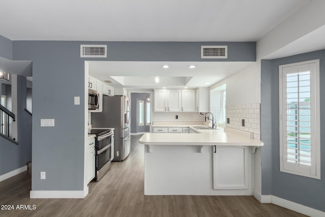 kitchen featuring kitchen peninsula, appliances with stainless steel finishes, a kitchen bar, decorative backsplash, and white cabinets