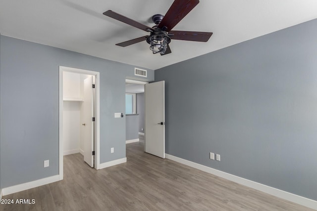 unfurnished bedroom with a walk in closet, ceiling fan, a closet, and light hardwood / wood-style floors