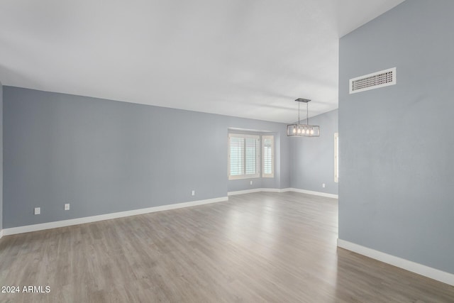 empty room featuring wood-type flooring and an inviting chandelier