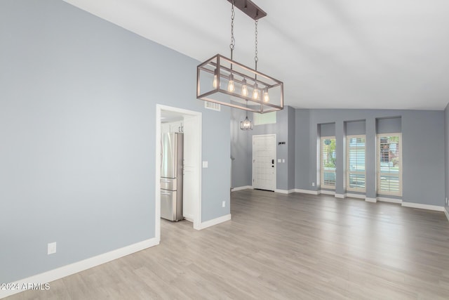 empty room featuring a chandelier, lofted ceiling, and light wood-type flooring