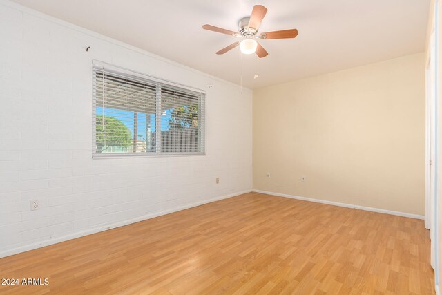 spare room featuring light wood-type flooring, ceiling fan, ornamental molding, and brick wall