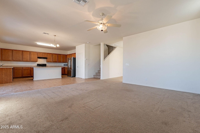 interior space featuring light carpet, a kitchen island, hanging light fixtures, and stainless steel refrigerator