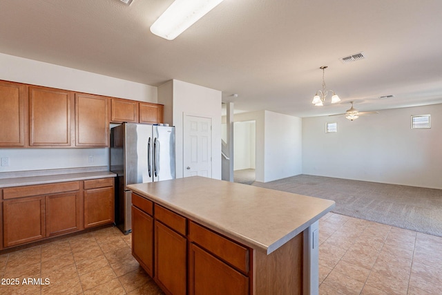 kitchen featuring stainless steel fridge, pendant lighting, ceiling fan with notable chandelier, and a kitchen island