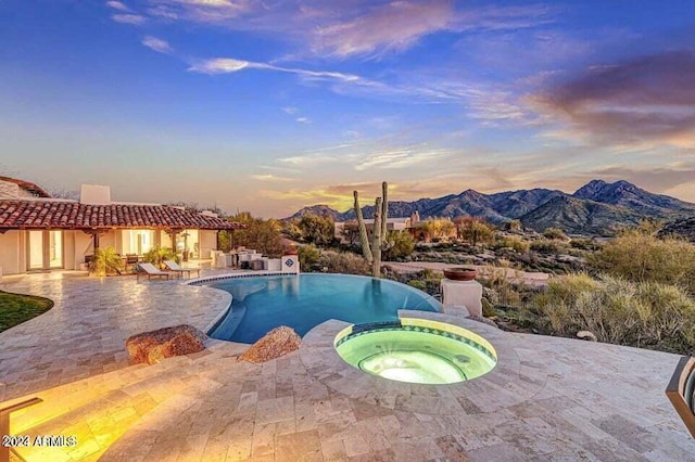 pool at dusk with a patio area, an in ground hot tub, and a mountain view