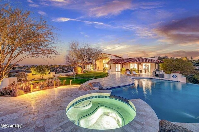 pool at dusk with a patio and an in ground hot tub