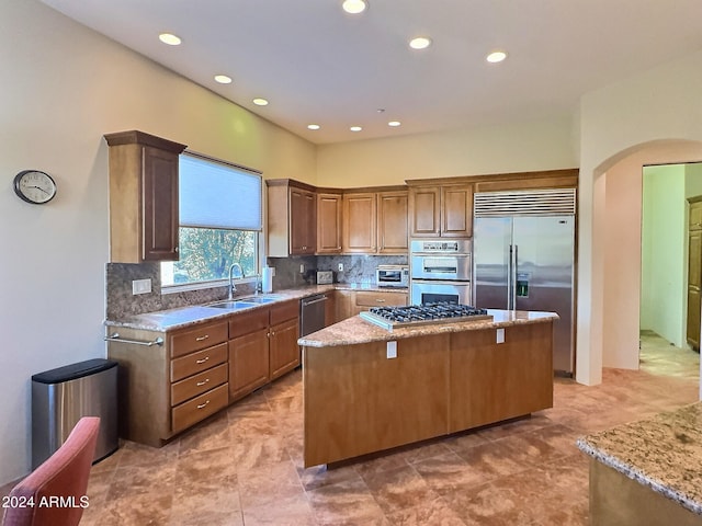 kitchen featuring a kitchen island, backsplash, appliances with stainless steel finishes, light stone countertops, and sink