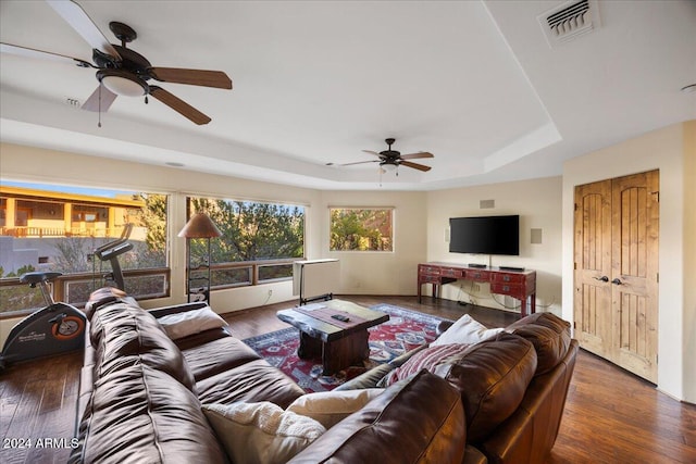 living room with dark hardwood / wood-style flooring, ceiling fan, and a raised ceiling