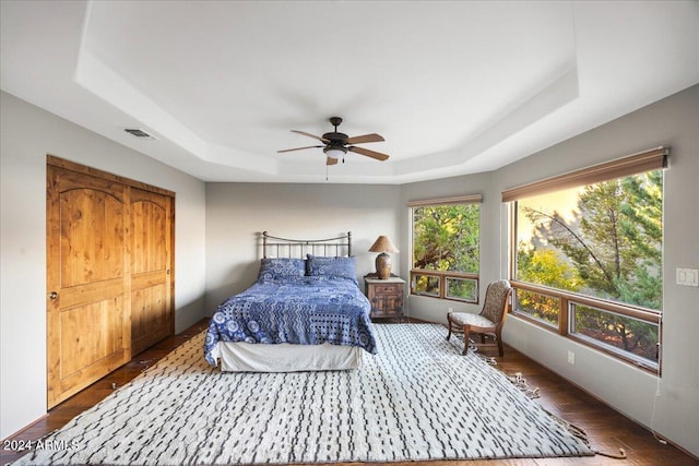 bedroom with dark wood-type flooring, ceiling fan, and a tray ceiling