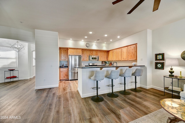 kitchen with kitchen peninsula, ceiling fan, stainless steel appliances, hardwood / wood-style flooring, and a breakfast bar area