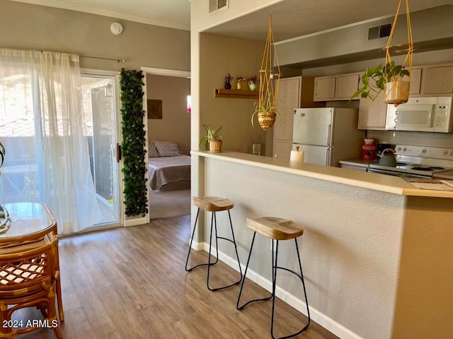 kitchen with crown molding, white appliances, a kitchen bar, light brown cabinetry, and light wood-type flooring